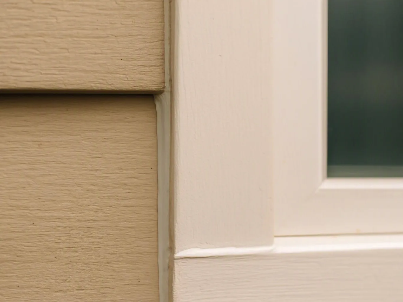 Close-up of beige siding meeting a white window frame beside dark glass