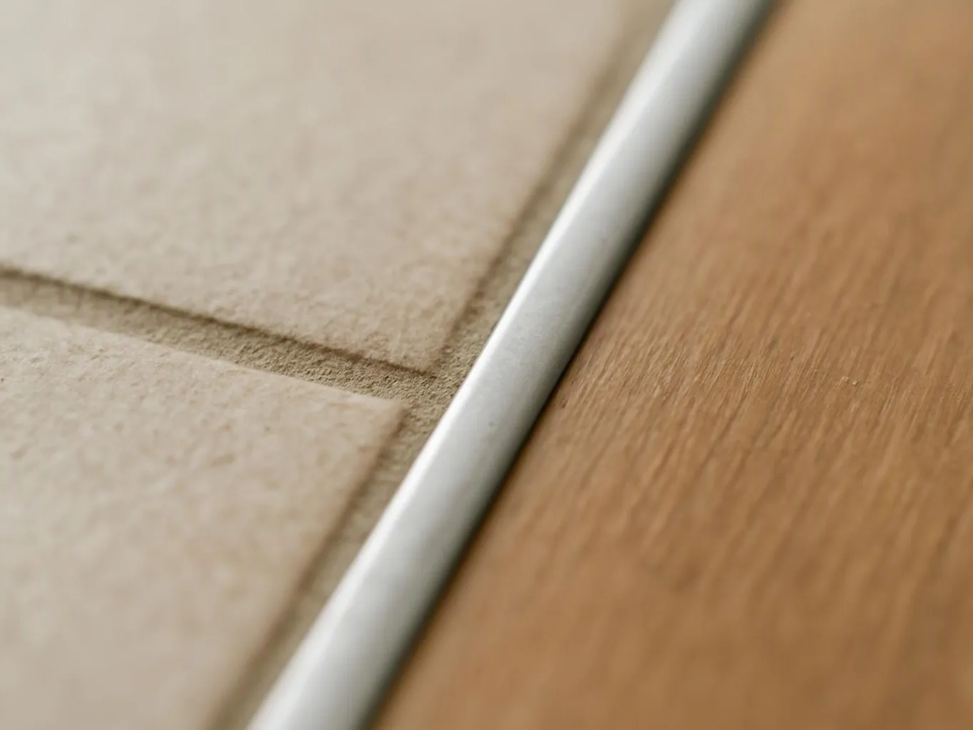 Close-up of a beige textured surface beside a white metal strip and a wooden floorboard