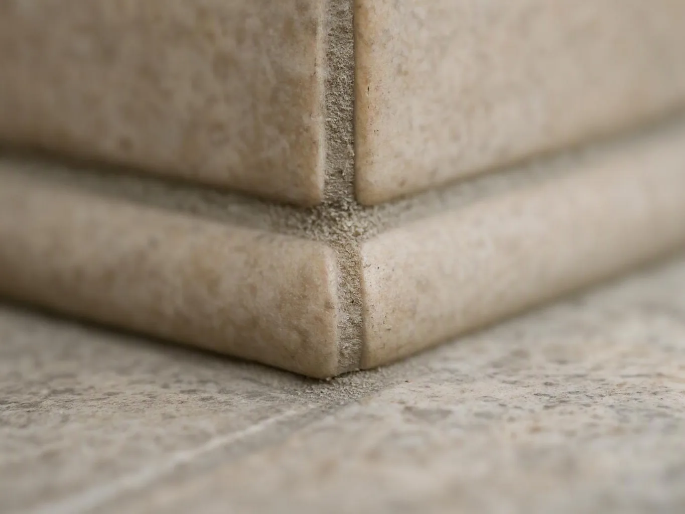 Close-up of beige tiled corners meeting with gray grout on a speckled stone floor
