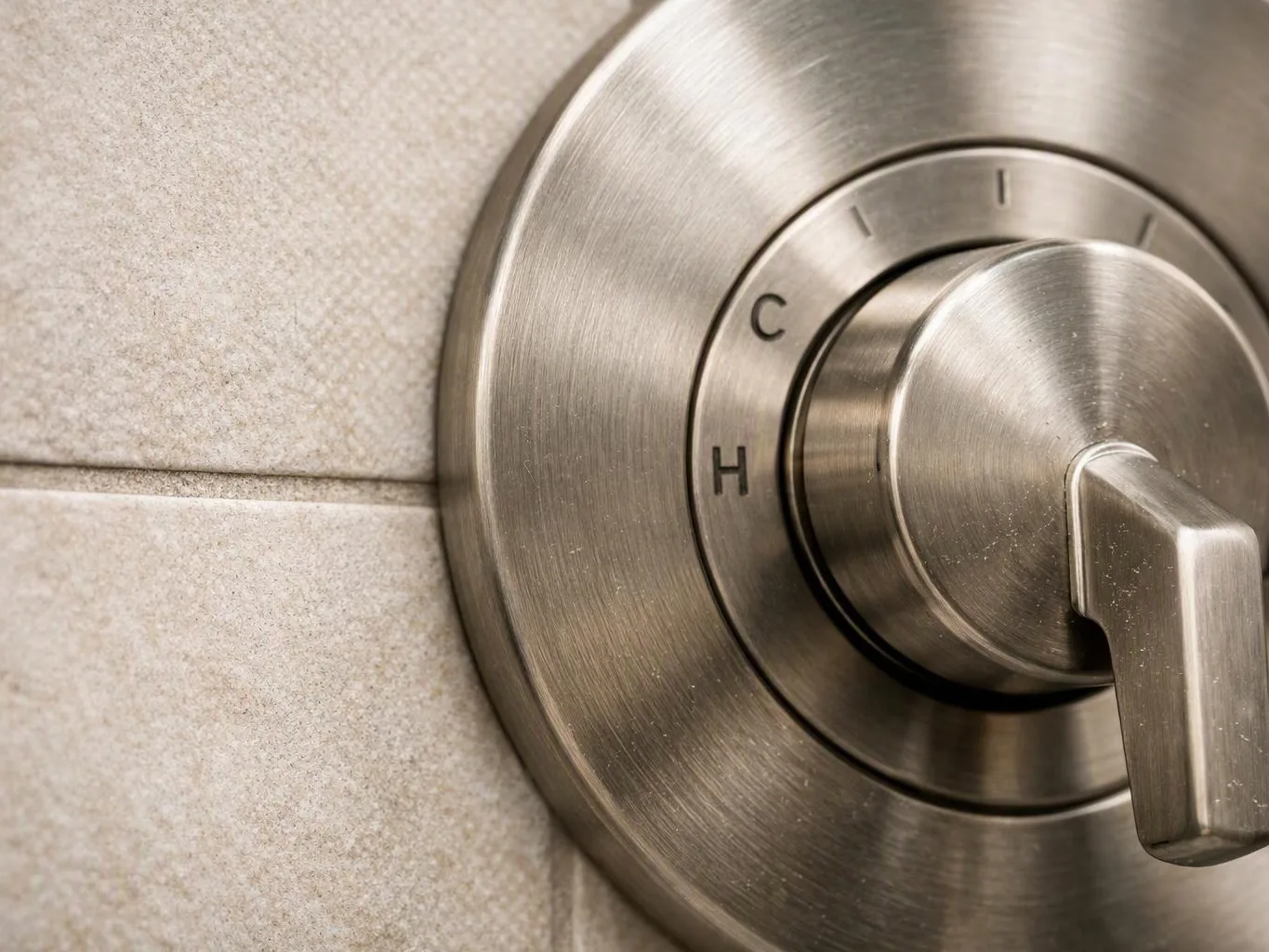Close-up of a brushed metal shower control knob mounted on beige tile wall
