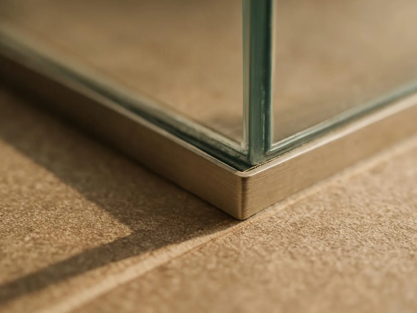 Close-up of a glass panel corner in a brushed metal frame on a textured surface