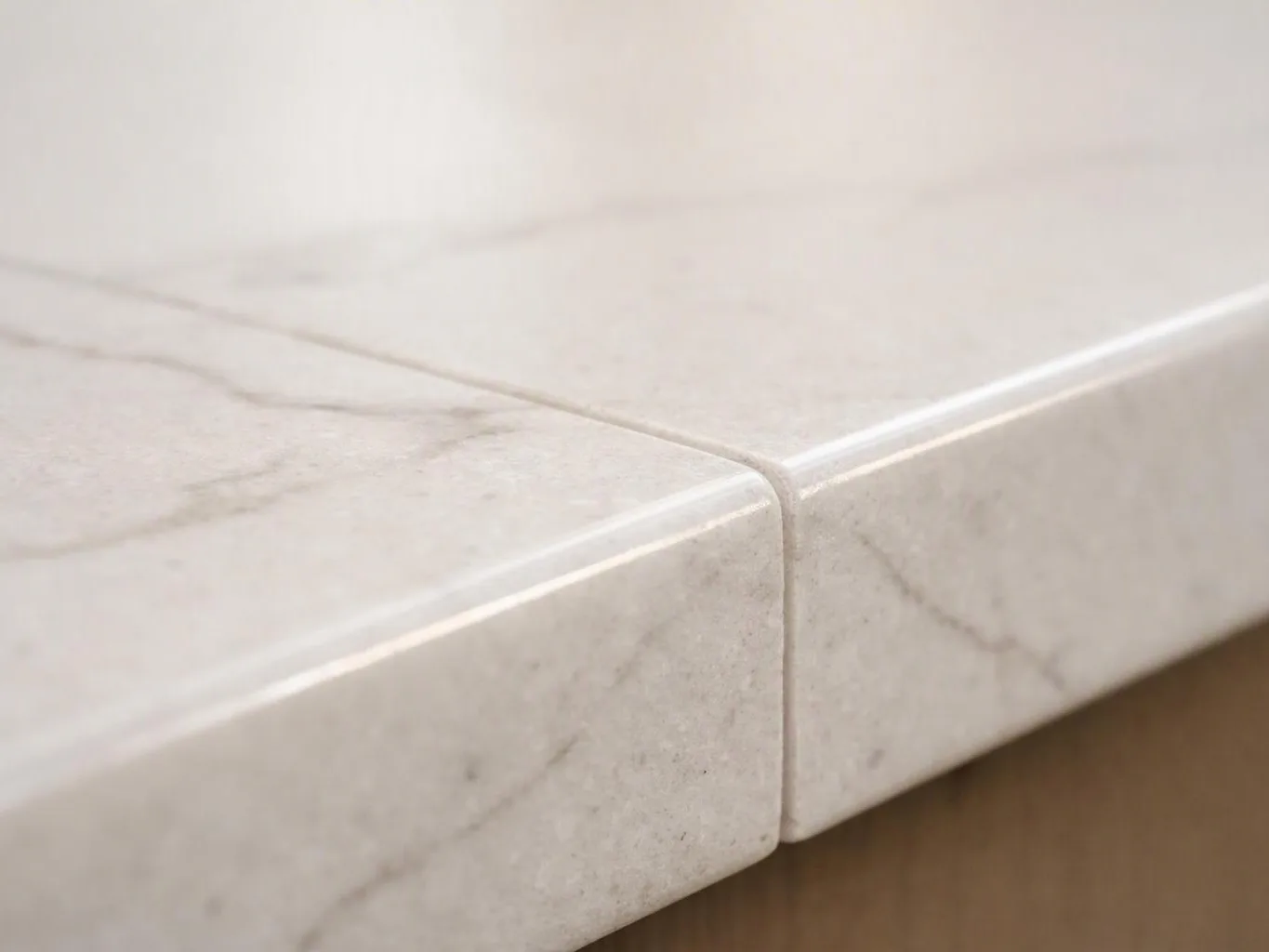 Close-up of a light marble countertop edge with a rounded corner and visible veining against a blurred background