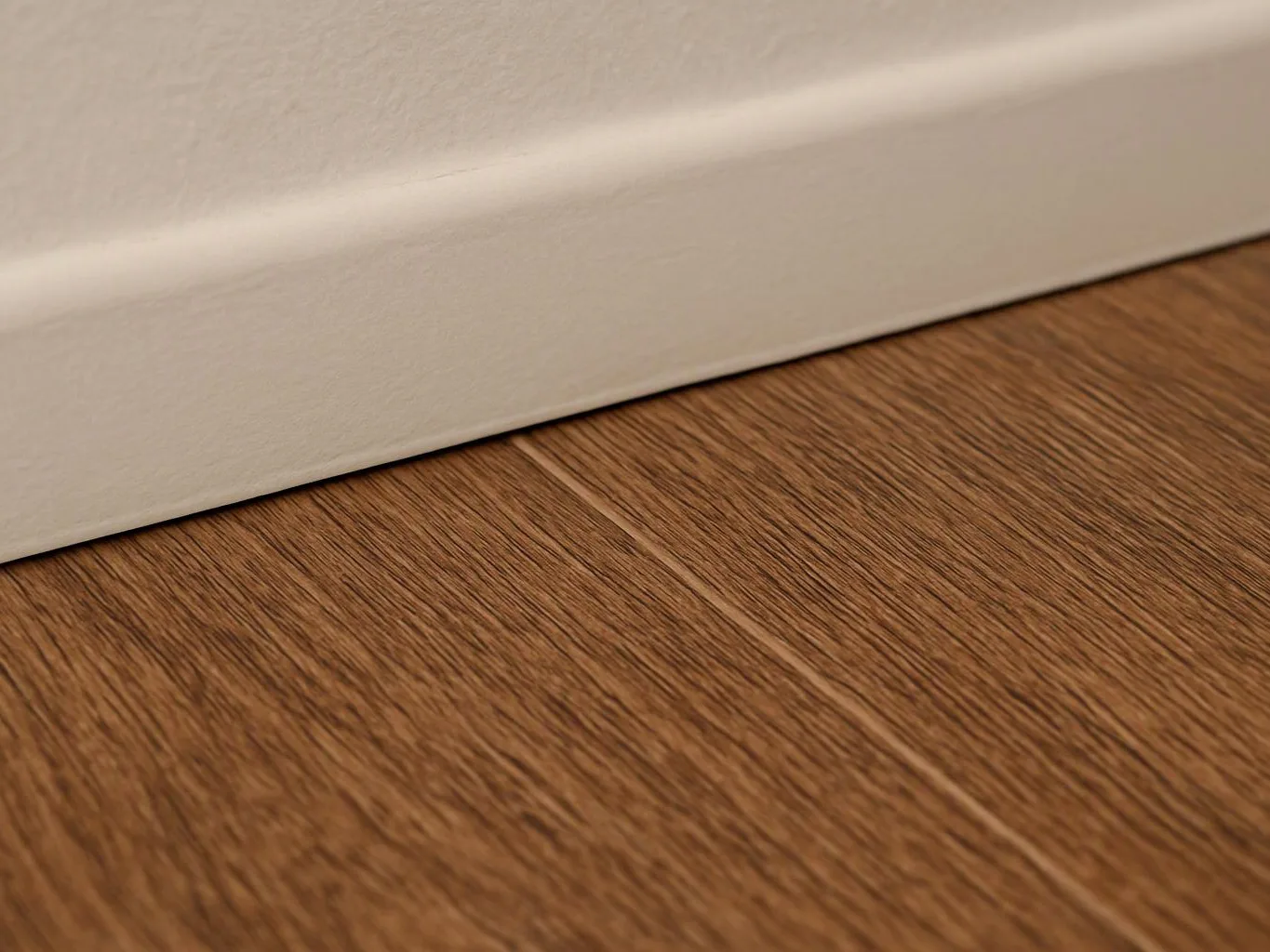 Close-up of a white baseboard above a wood floor with visible grain textures