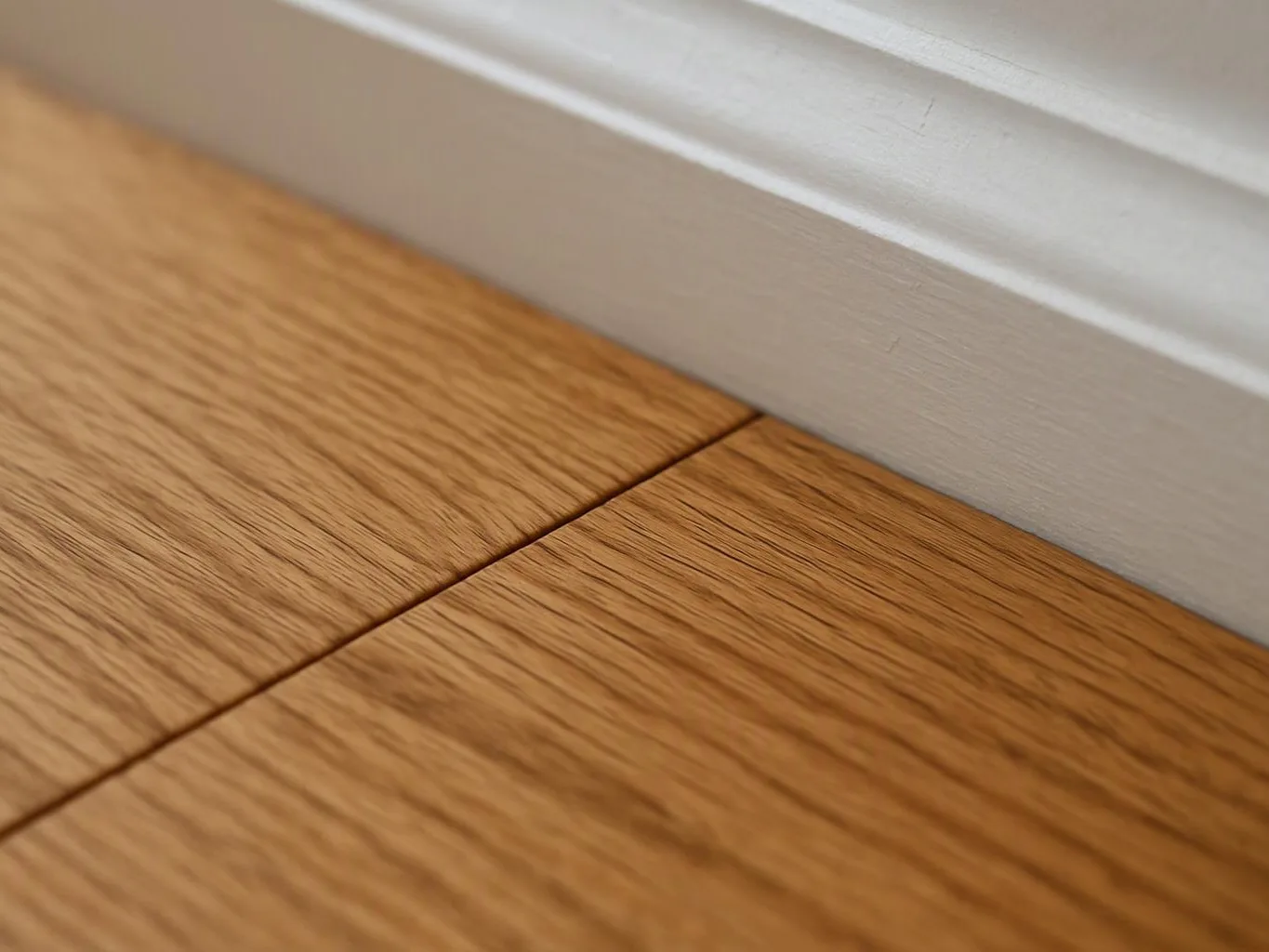 Close-up of wood floor boards meeting a white baseboard along the wall