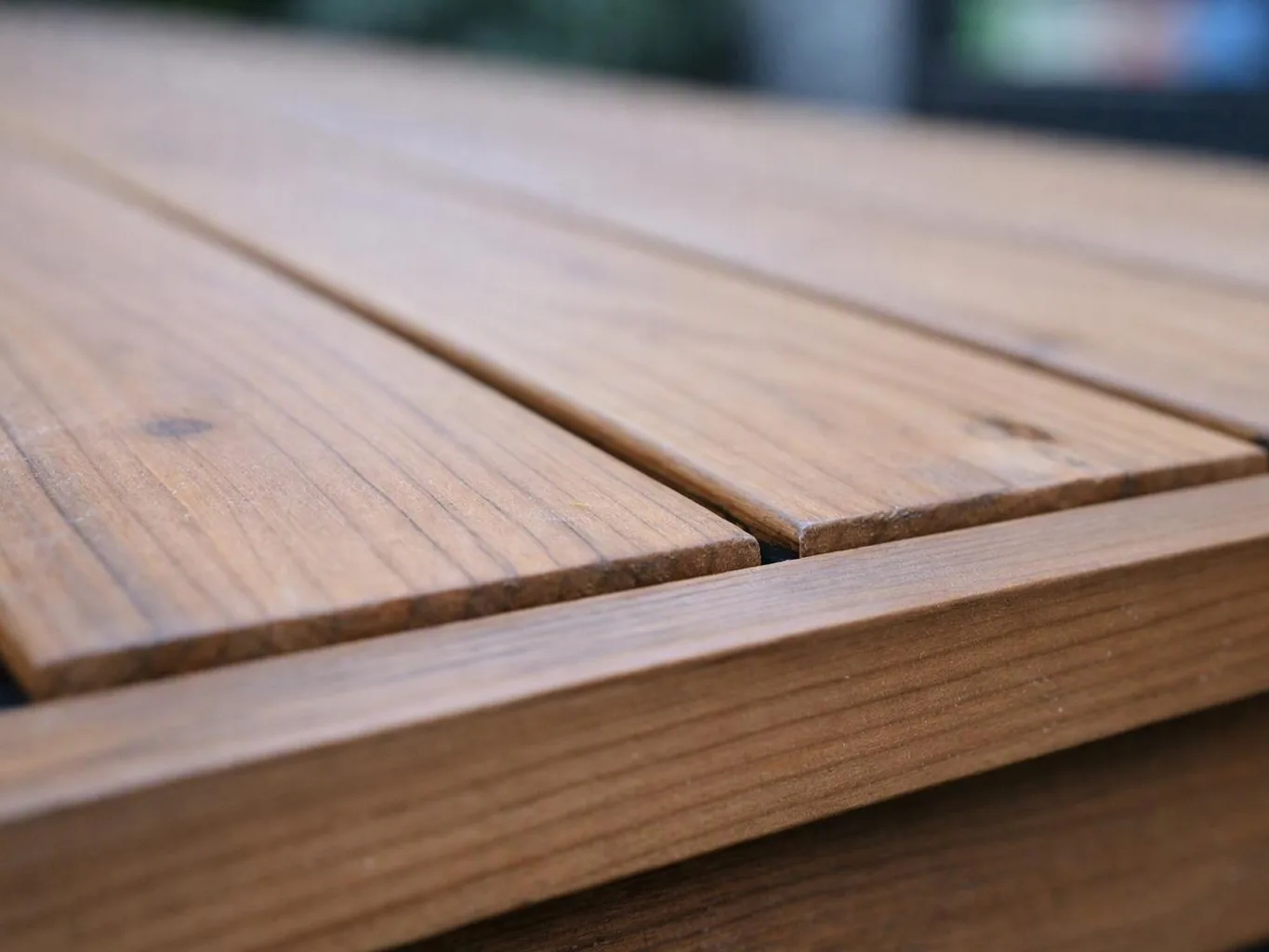 Close-up of a wooden tabletop with narrow slats and a blurred background