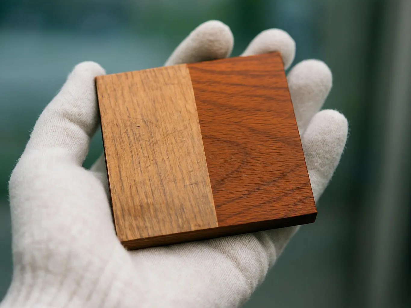 A gloved hand holds a square wood sample with two different grain patterns against a blurred background