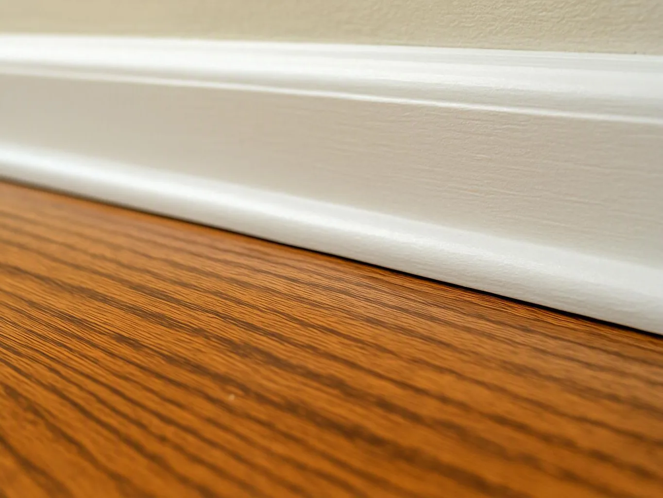 White baseboard meets a wood floor against a beige wall, shown in close-up
